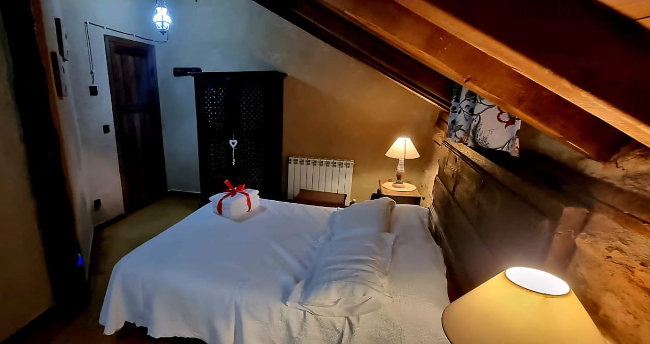 Dormitorio rústico señorial de la Suite Sepúlveda con pared de piedra en MaderoluM